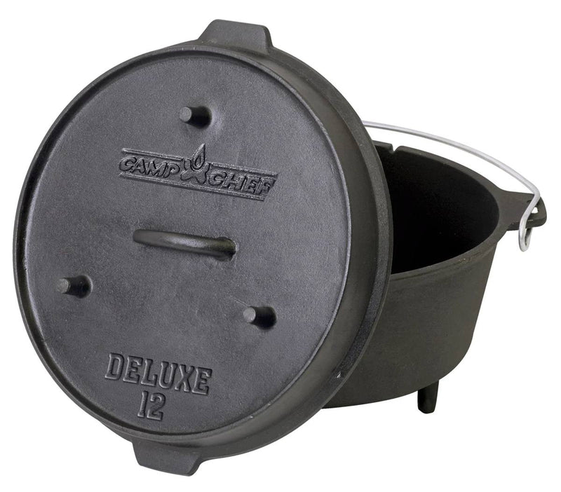 Load image into Gallery viewer, The Camp Chef Deluxe Dutch Oven is a black cast iron pot with three short legs, a metal handle, and a partially open lid leaning against it.
