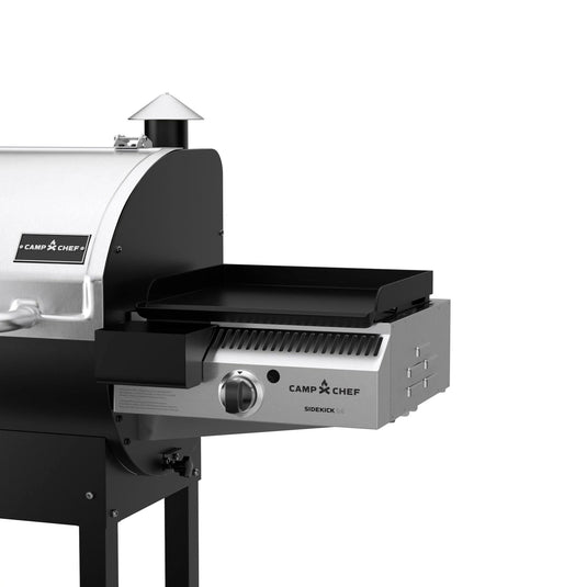 A close-up of the Camp Chef Sidekicks, a versatile pellet grill accessory with stainless steel and black accents, highlights the propane burner on the right side of this flat-top griddle attachment.