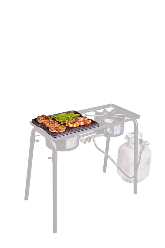 The Camp Chef Griddles 14 propane camp stove, equipped with metal legs, a side shelf, and a heat diffuser plate, is shown cooking chicken, asparagus, and veggie skewers on its pre-seasoned griddle with a connected propane tank.