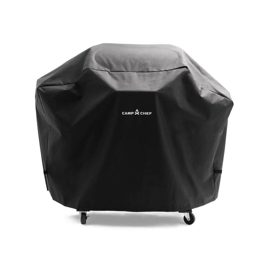 A Camp Chef Woodwind Pro Cover in black with a bold white logo protects your grill from dust and weather. The cover fits over a four-wheeled grill, keeping your Camp Chef appliance safe outdoors.