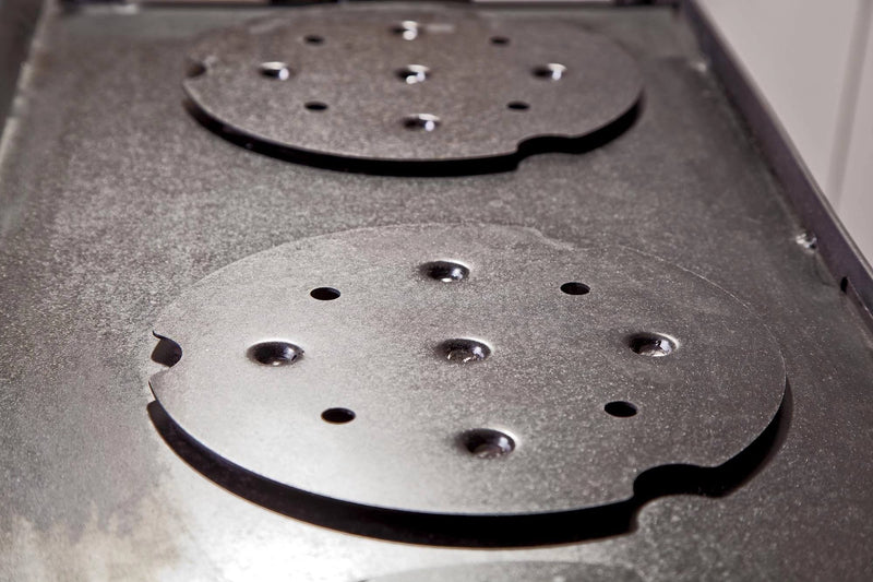 Load image into Gallery viewer, Close-up of a metal stovetop with two round, removable hot plates featuring holes and notches on a textured surface—ideal for use with the Camp Chef Griddles 16 or other professional griddle setups.
