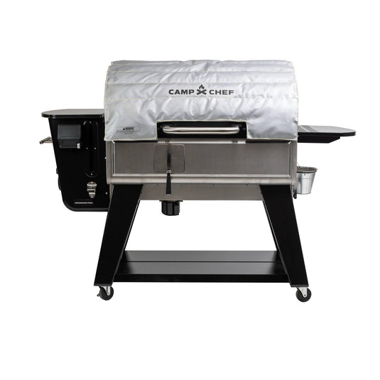 The Camp Chef Woodwind Pro with a silver, fire-resistant Woodwind Pro Blanket on the lid features a black frame, side shelves, and wheels for mobility.