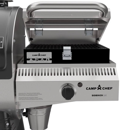 A close-up of a Camp Chef Sidekick Sear outdoor grill with its lid open displays the black grill grate and front control knob, ideal for pairing with your Camp Chef Woodwind 24 pellet grill and WIFI controller for added convenience.