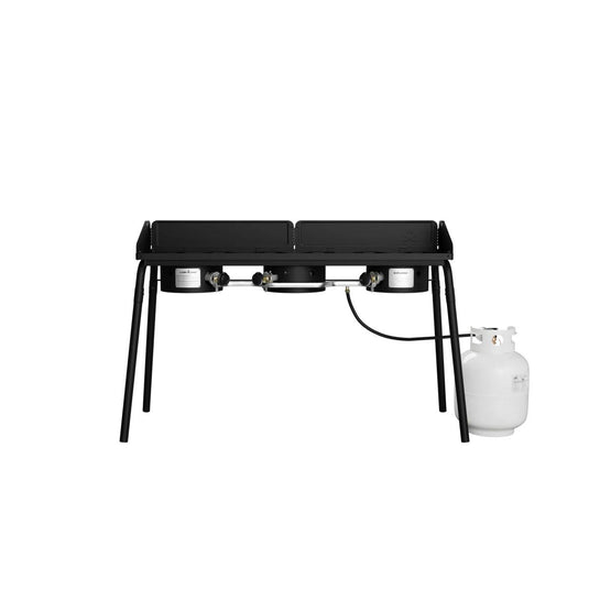 The Camp Chef Explorer is a black, two-burner outdoor propane gas stove with four legs and a white propane tank, ideal for outdoor cooking. Shown on a plain white background.
