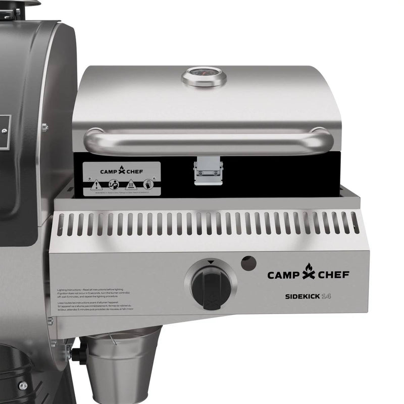 Load image into Gallery viewer, A close-up of a Camp Chef Sidekick Sear attached to a Camp Chef Woodwind 24 grill, highlighting the stainless steel lid with temperature gauge, control knob, and the Camp Chef logo on the front panel.
