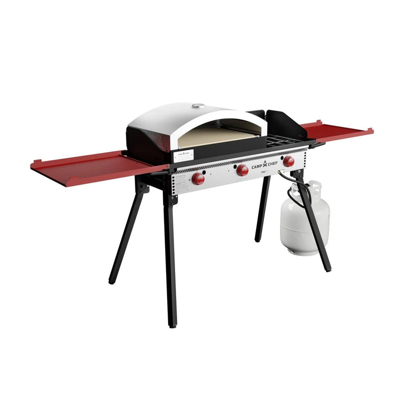 Load image into Gallery viewer, The Camp Chef Pizza Oven 16 - 2 Burner is a portable outdoor gas grill with an artisan pizza oven and ceramic stone, red control knobs, two foldable red side shelves, black legs, and a connected white propane tank.
