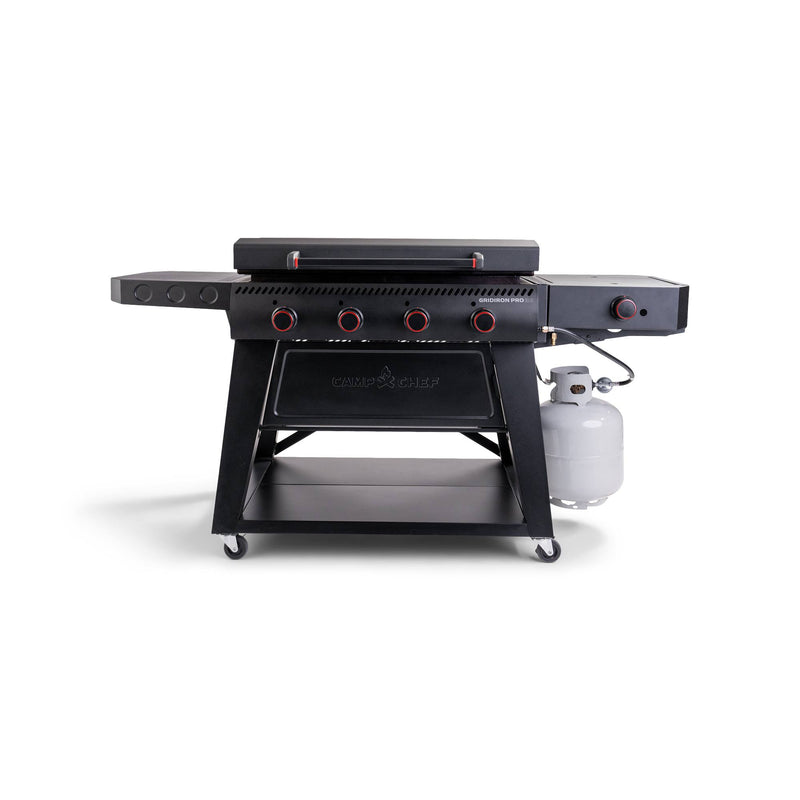 Load image into Gallery viewer, The Camp Chef Gridiron Pro Flat Top Grill is a large black outdoor cooker with multiple red knobs, a side burner, storage shelf, and right-side propane tank, all set on wheels for easy mobility.

