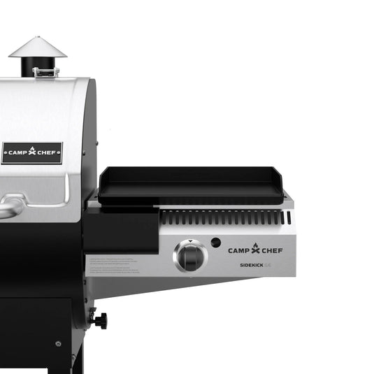 Close-up of a Camp Chef grill with the Camp Chef Sidekicks propane burner and flat top griddle, showing part of the main grill and the attached pellet grill accessory on the right.