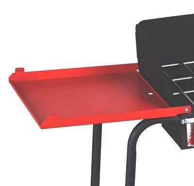 A close-up of the Camp Chef Stove - Side Shelf Set in red, attached to a black grill, with part of the grill grate and frame visible—ideal for adding extra prep space to your outdoor cooking setup.