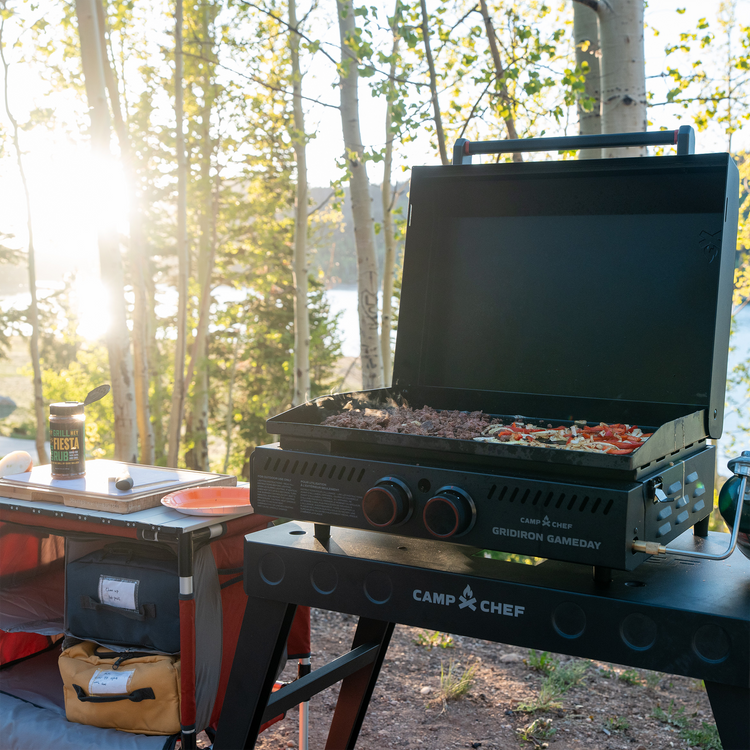 Camp Chef grill on a camping setup with trees and sunset in the background