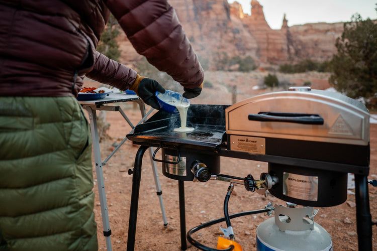 Person preparing food on a portable stove outdoors with scenic background
