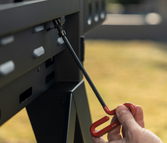 Person using a red screwdriver to tighten screws on a metal frame outdoors.