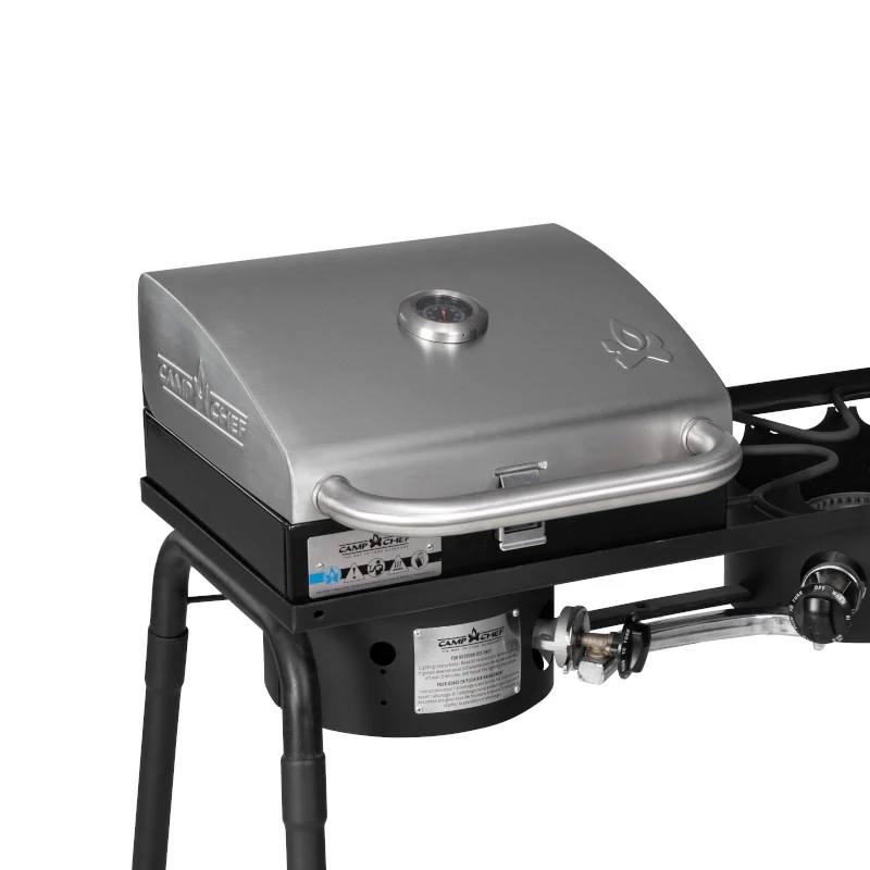 Load image into Gallery viewer, The Camp Chef BBQ Grill Boxes 14 is a stainless steel tabletop grill with a closed lid, handle, temperature gauge, and control knobs. Mounted on black metal legs, it has a cast iron grilling surface and gas burner for excellent heat retention.

