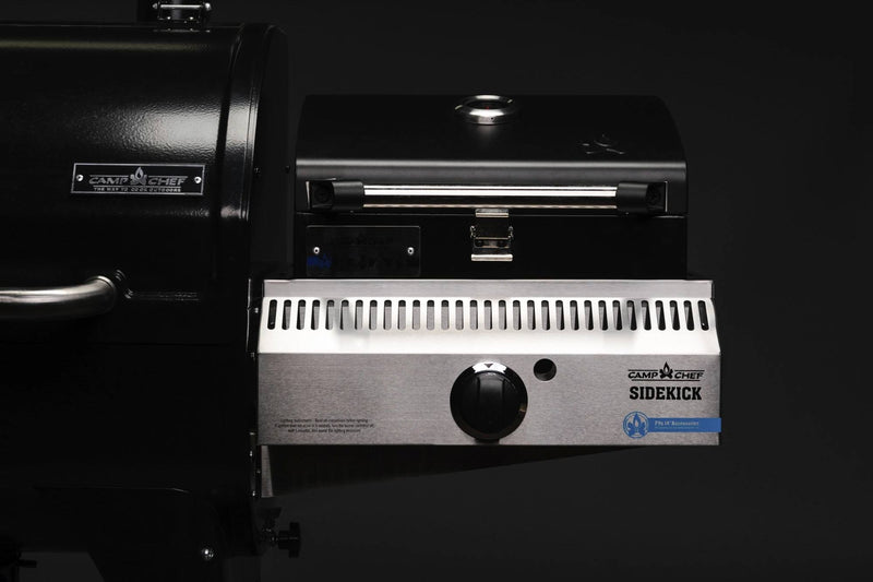 Load image into Gallery viewer, A close-up of a Camp Chef Sidekicks accessory shows the control knob, branding, and part of the main grill against a dark background.
