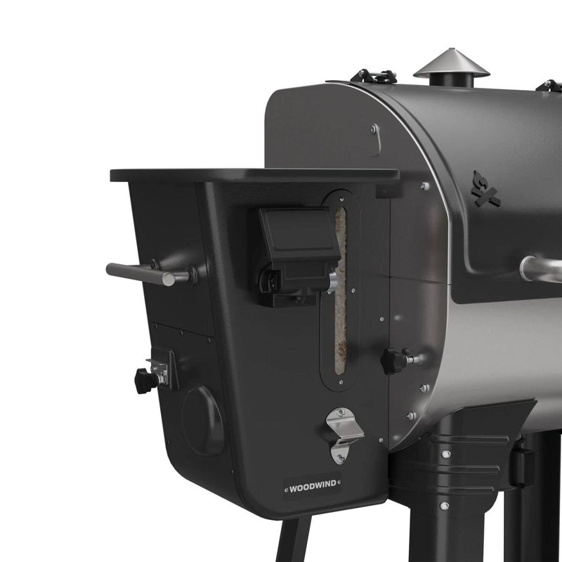Load image into Gallery viewer, Close-up of the Camp Chef Woodwind 24 pellet grill in black and silver, highlighting the hopper with visible pellets and the WIFI controller. The unit includes a sturdy handle and multiple control knobs for easy operation.
