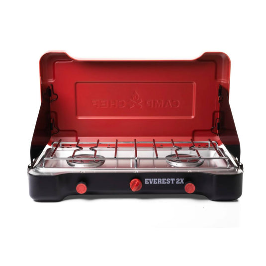 The Camp Chef Everest 2X is a portable stove with two burners, dual control knobs, metal grates, and a red lid embossed with the brand—ideal for outdoor cooking on camping trips.