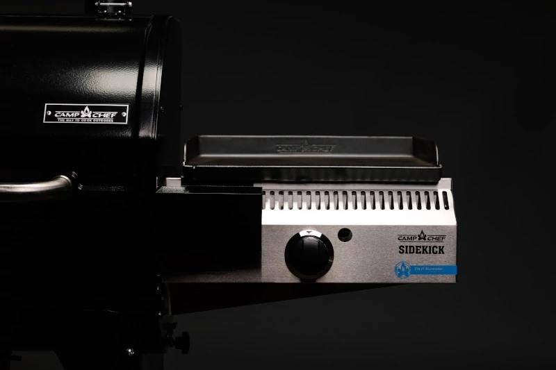 Load image into Gallery viewer, A close-up of the Camp Chef Sidekicks grill attachment, a versatile accessory featuring a black grill surface and control knob, set against a dark background.

