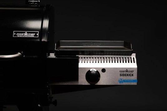 A close-up of the Camp Chef Sidekicks grill attachment, a versatile accessory featuring a black grill surface and control knob, set against a dark background.