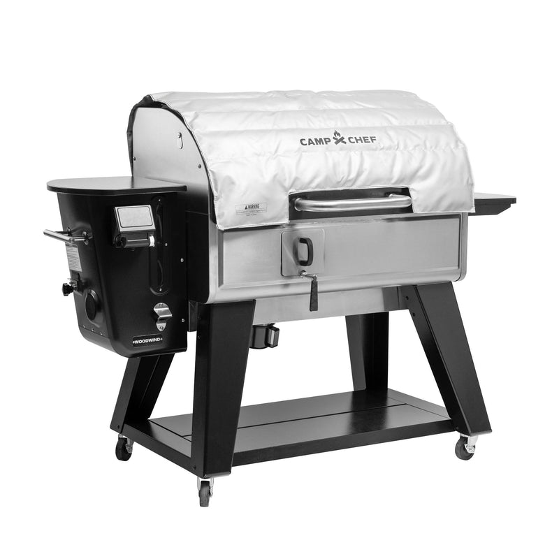 Load image into Gallery viewer, The Camp Chef Woodwind Pro Blanket is a fire-resistant white fiberglass cover for the stainless steel Woodwind grill, featuring a black frame, left-side control panel, and four wheels for easy mobility.
