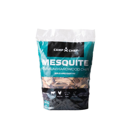 A bag of Camp Chef Wood Chips with a teal and black label showing food images and "Bold and Earthy" text. The clear bottom displays premium hardwood BBQ wood chips inside.
