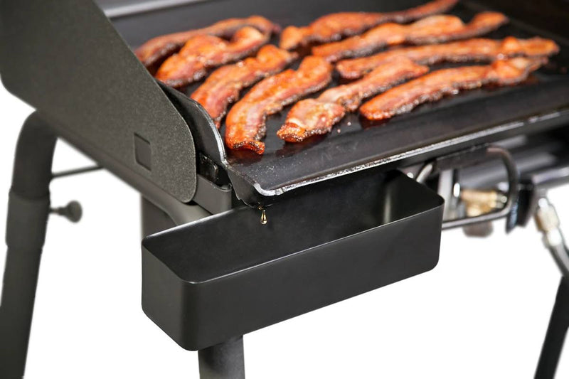 Load image into Gallery viewer, Close-up of sizzling bacon strips cooking on a griddle, with grease draining efficiently into the Camp Chef Professional Grease Cup below for optimal management.
