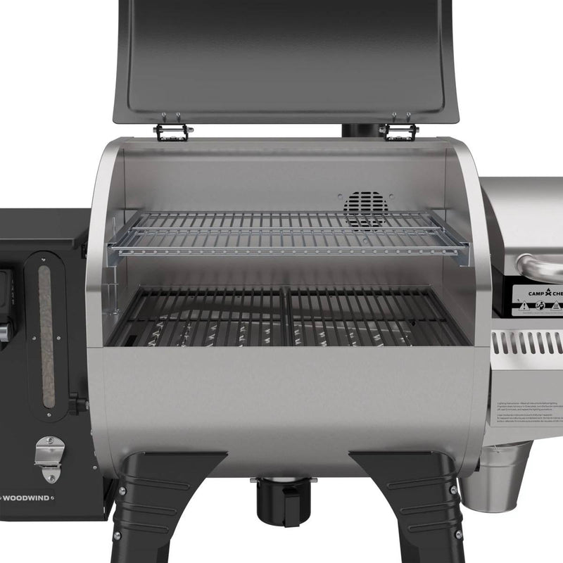 Load image into Gallery viewer, A close-up of the Camp Chef Woodwind 24 pellet grill with its lid open, displaying black grates on the main area and a raised second rack. This stainless steel grill features sturdy legs, metal parts, and a WIFI controller for easy use.
