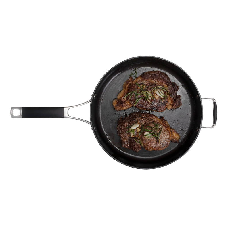 Load image into Gallery viewer, A top-down view of the Camp Chef Heritage Skillets, a black cast iron frying pan with black and metal handles, featuring two cooked steaks garnished with rosemary and garlic, renowned for excellent searing, set against a white background.
