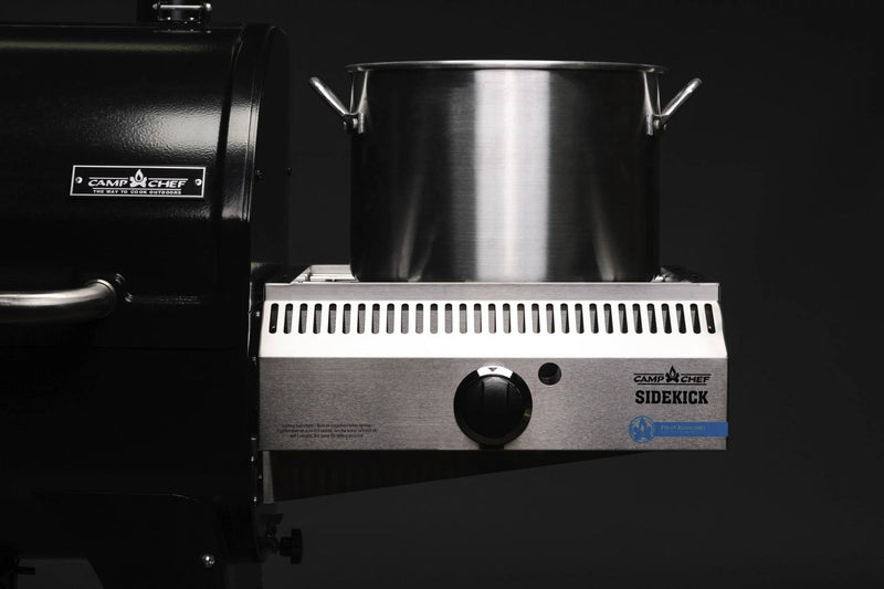 Load image into Gallery viewer, A large stainless steel pot sits on the propane burner of a black Camp Chef Sidekicks, a versatile grill accessory, against a dark background.
