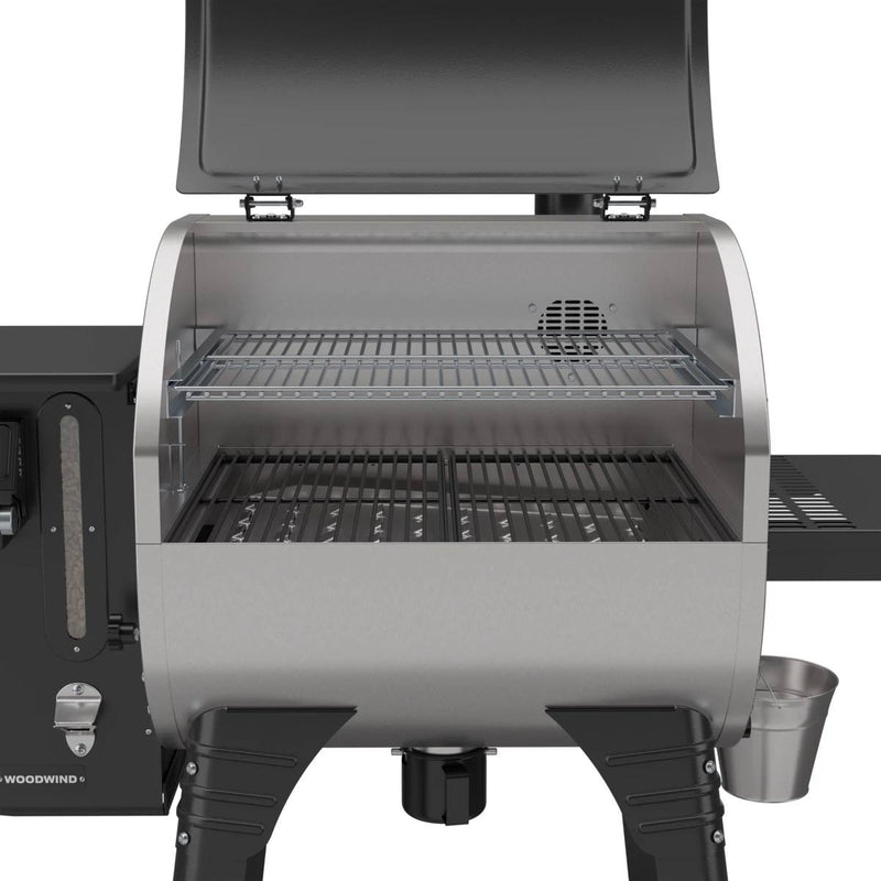 Load image into Gallery viewer, The Camp Chef Woodwind 24 pellet grill, shown with the lid open and two cooking racks, features a WIFI controller, black legs, and a side shelf with a silver bucket—making outdoor grilling easy and convenient.
