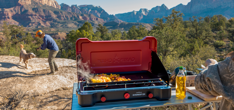 Outdoor cooking setup with a portable stove and food on a scenic mountain backdrop