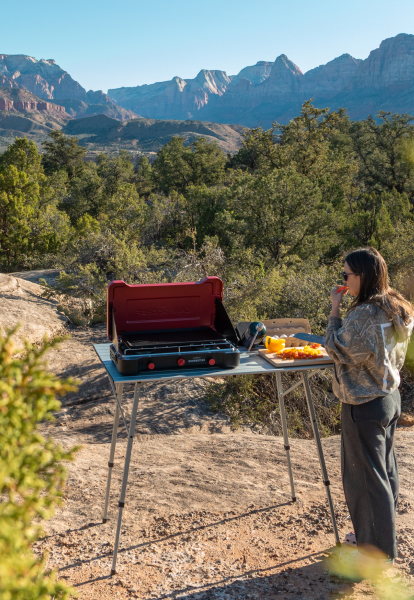 Person cooking outdoors with a portable stove and table in a mountainous area