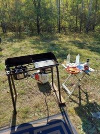 Outdoor cooking setup with portable stove and small table in a forested area