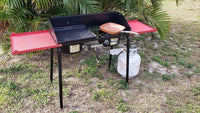 Portable grill with red trays on a grassy outdoor area