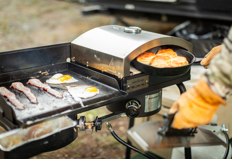 Portable outdoor grill with griddle and pizza oven cooking food outdoors.