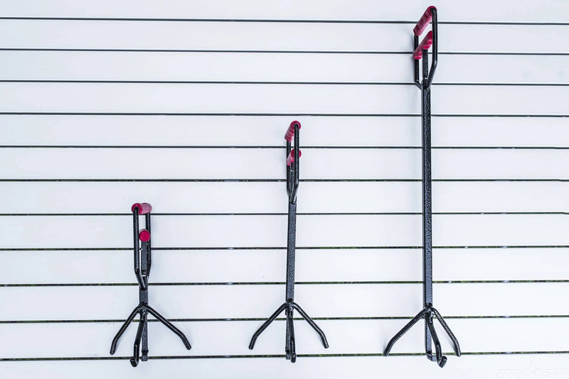 Load image into Gallery viewer, Three Camp Chef Dutch Oven Lid Lifters in varying lengths, with black shafts and red handles/tips, hang vertically on a white slatted wall—ideal for lifting cast iron lids, arranged shortest to tallest.
