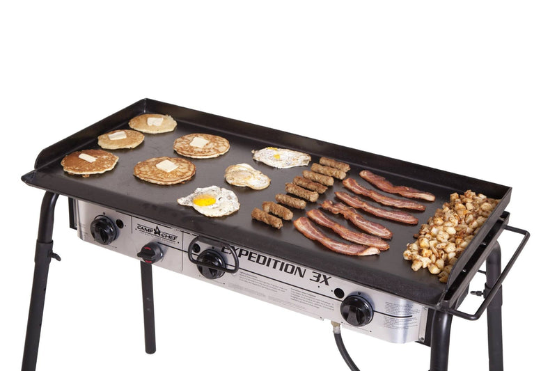 Load image into Gallery viewer, The Camp Chef Griddles 16, a large flat top with three control knobs and four sturdy legs, cooks pancakes, eggs, sausage links, bacon, and diced potatoes in neat rows—ideal for outdoor breakfasts.
