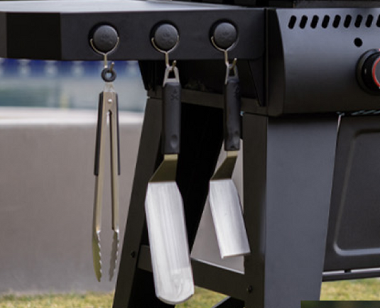 Barbecue tools hanging on a grill with a blurred background